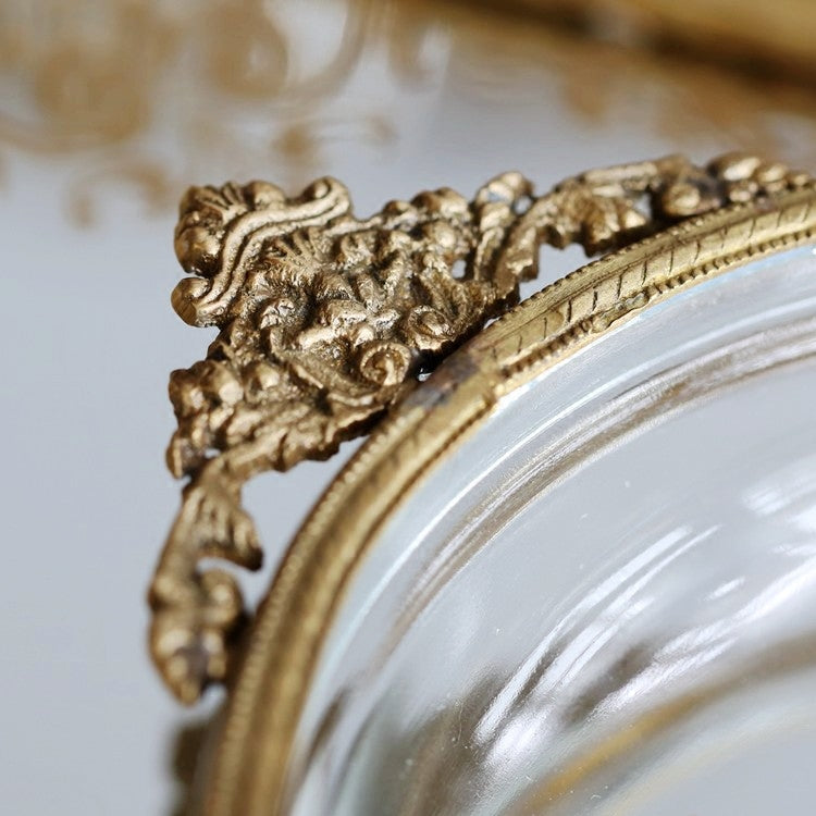 Brass-edged circular jewelry box with ornate gilt corner detailing and glass frame.