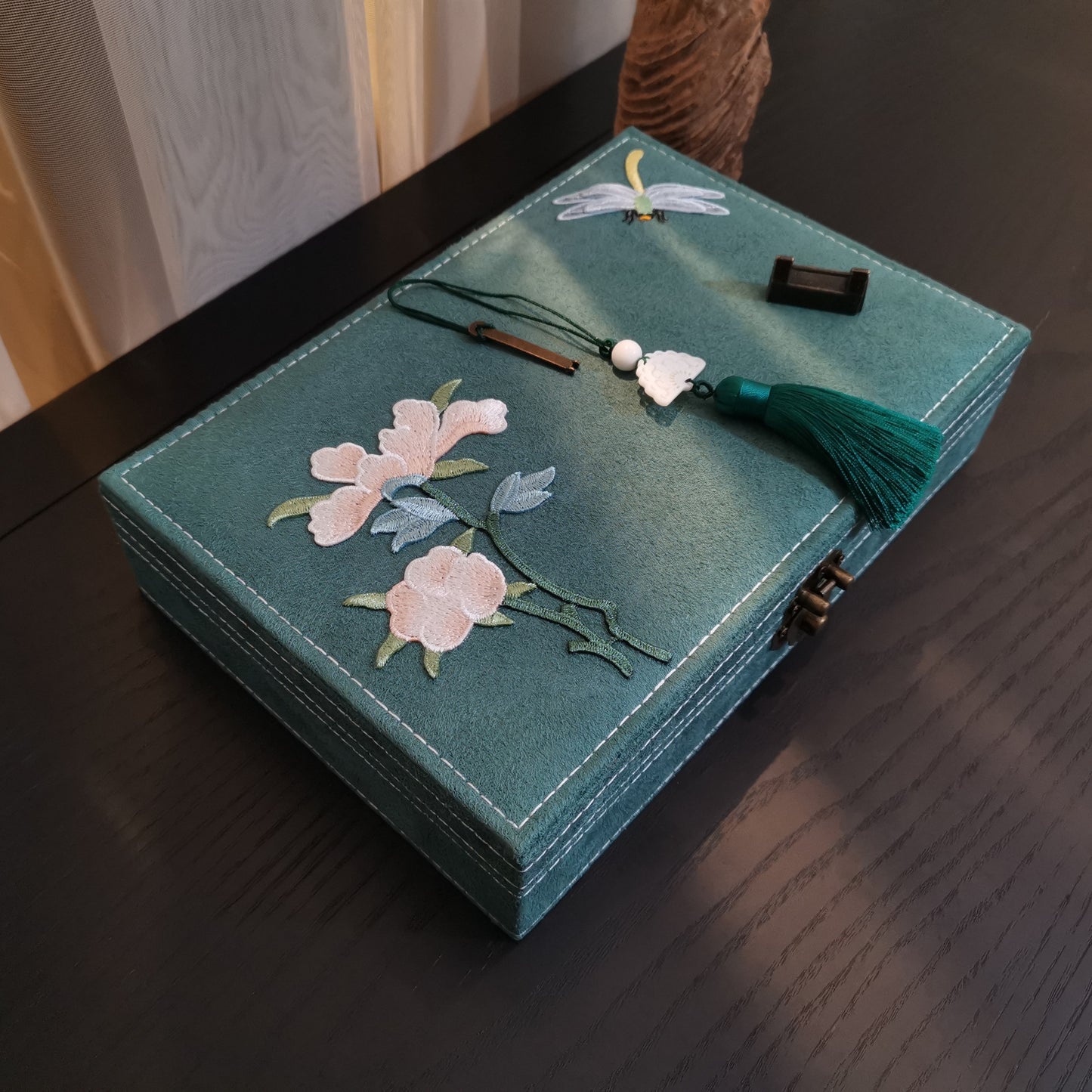 Teal flannel jewelry box with pink floral embroidery and a green tassel, metal latch