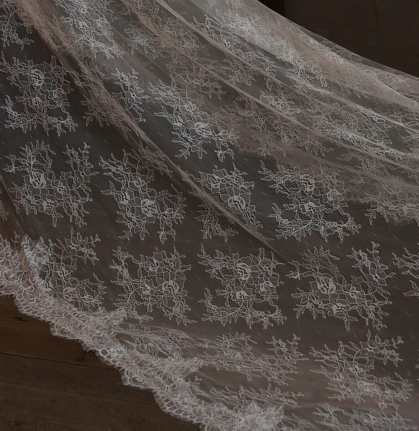 Close-up detail of white bridal veil fabric showing intricate floral lace pattern and delicate scalloped lace edge