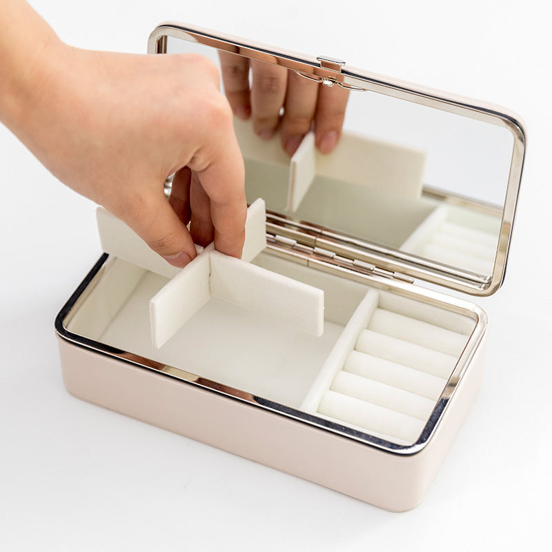 Jewelry storage box with mirror lid, rose-gold exterior and white foam inserts for rings and other jewelry.