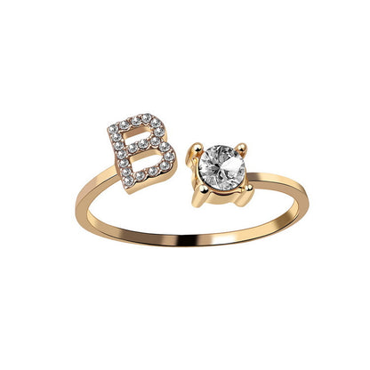 Gold ring with letter 'B' and heart-shaped diamond on a white background