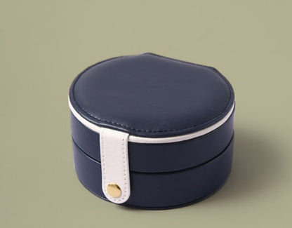 Portable jewelry box, round navy blue faux leather with white strap and gold button.