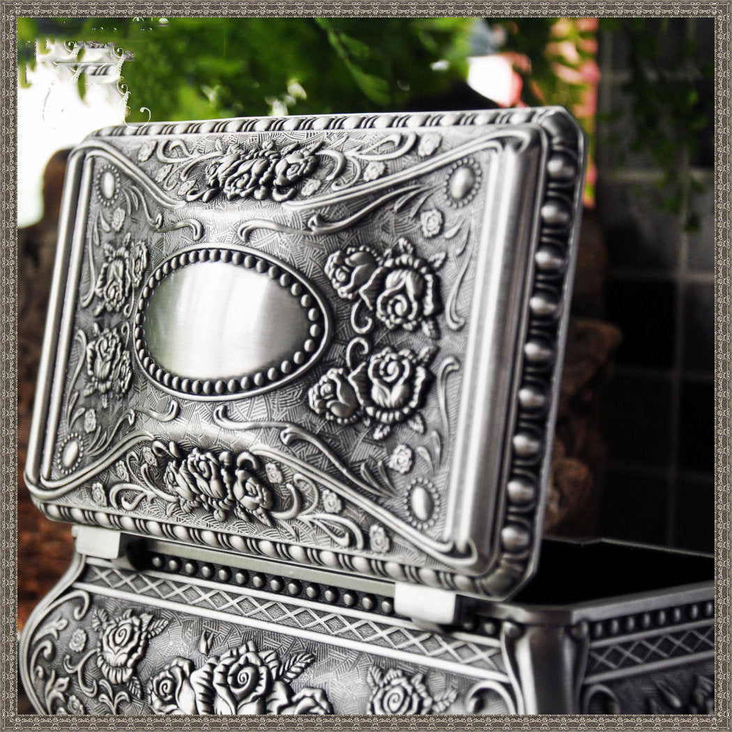 Vintage jewelry box with ornate embossed silver finish, floral relief and beaded border, open lid.
