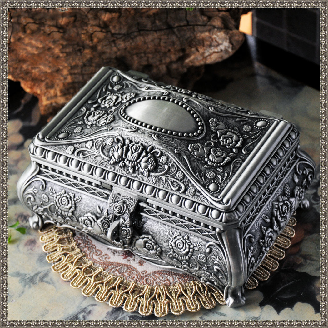 Vintage jewelry box in silver-tone metal with ornate floral embossing and decorative curved legs.