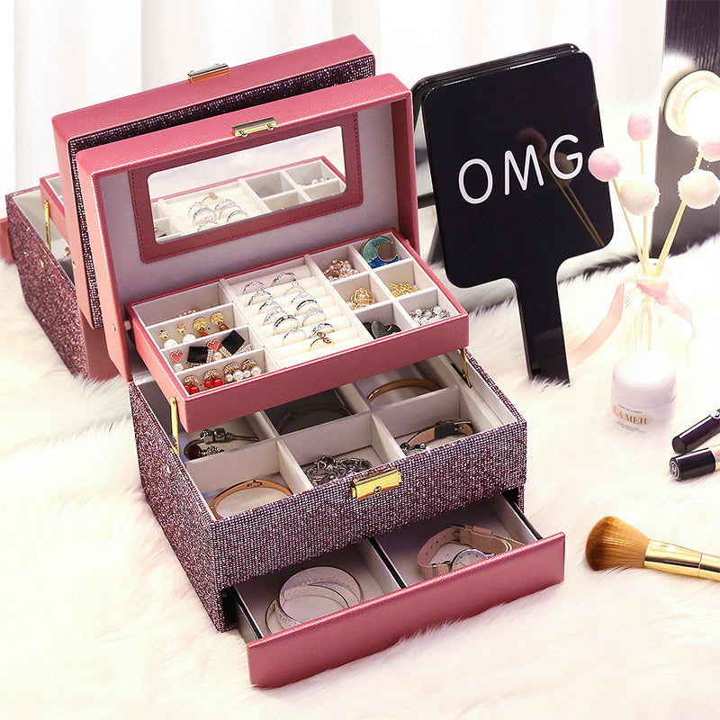 Organizing jewelry box in pink glitter finish with open trays and mirror, displaying rings and earrings.