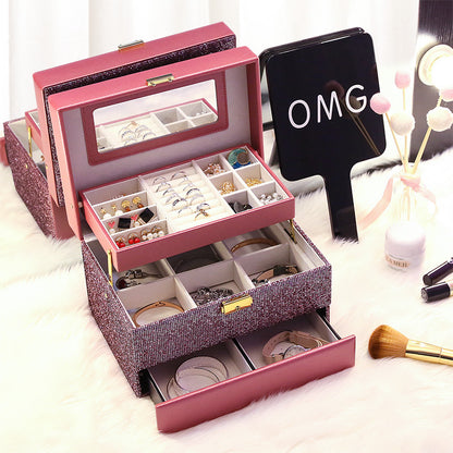 Organizing jewelry box in pink glitter finish with open trays and mirror, displaying rings and earrings.