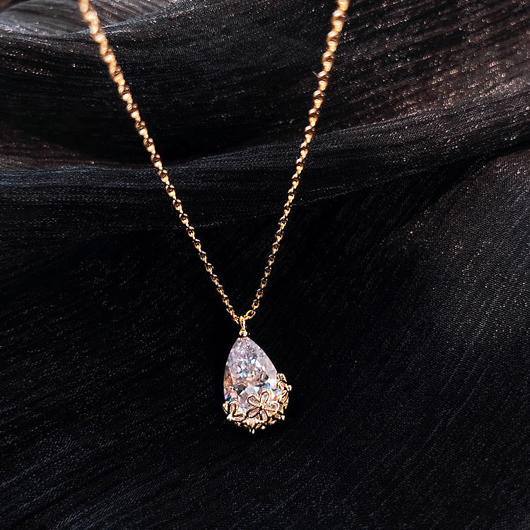 Crystal water drop pendant necklace in gold-tone with floral-lined setting on adjustable chain.