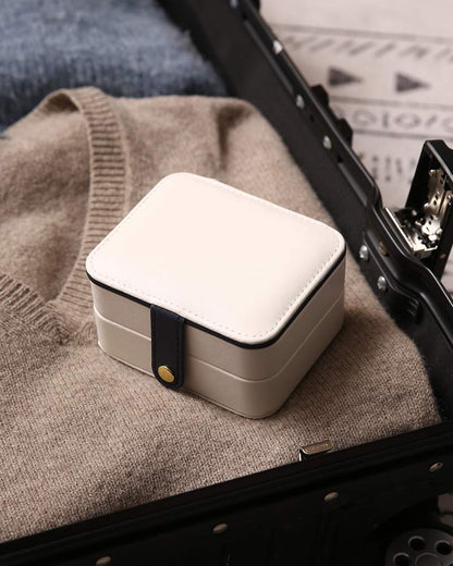 Portable jewelry box in cream-beige with white lid and navy strap.