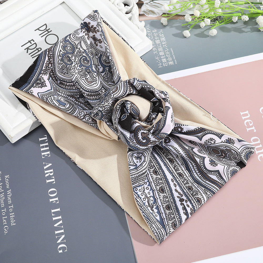Hairband silk scarf with intricate black-and-white paisley print on beige base, looped as a headband.