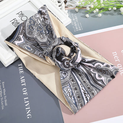 Hairband silk scarf with intricate black-and-white paisley print on beige base, looped as a headband.