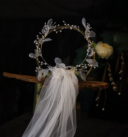 Bridal wreath crown with white tulle veil, gold-tone circular frame adorned with bead accents and translucent leaves.