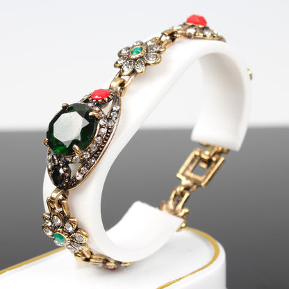 Vintage ethnic style bracelet with gold-tone metal and a large green central stone, accented by crystals.