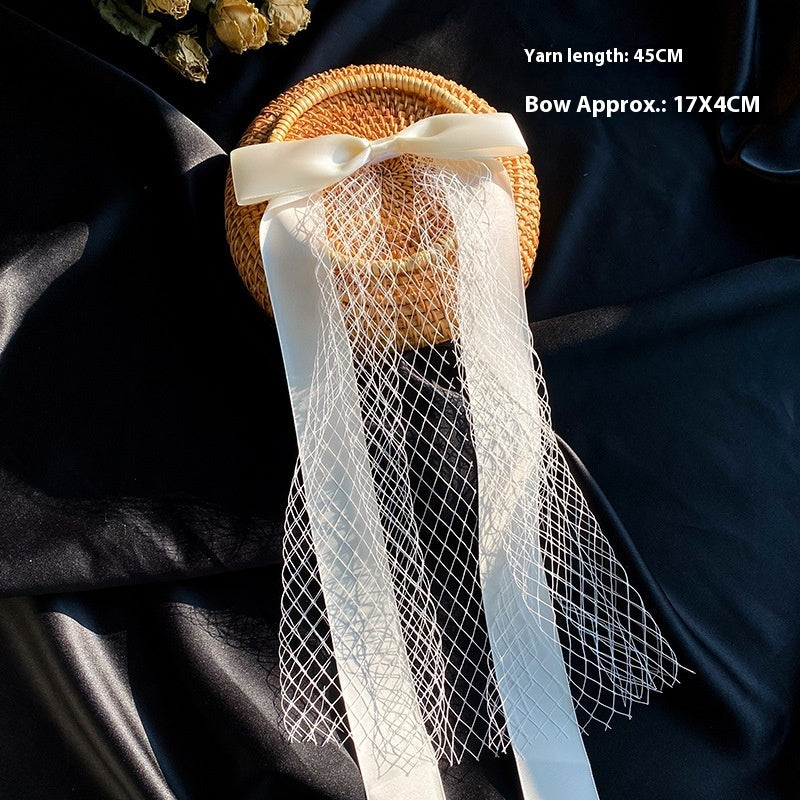 Bow veil wedding accessory featuring a straw hat with a white satin bow and net veil.