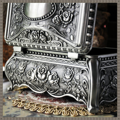 Vintage jewelry box with ornate silver-tone embossed floral pattern and curved legs