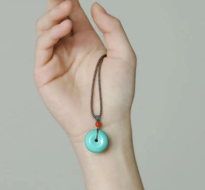 Turquoise donut pendant necklace with bronze chain and red accent bead.