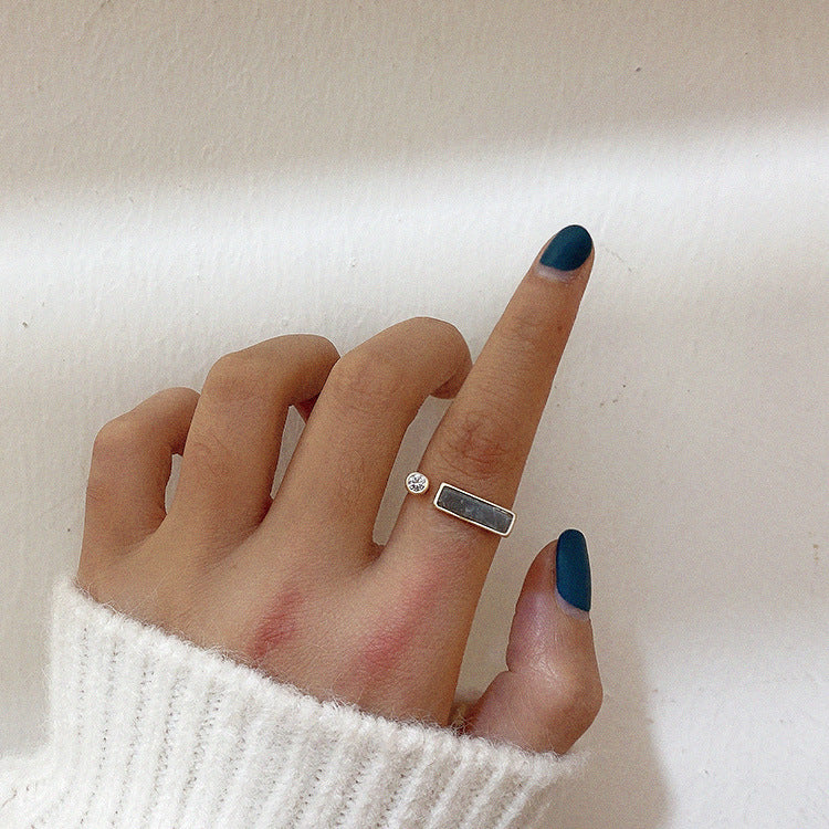 Hand with dark nail polish wearing two rings on a light background