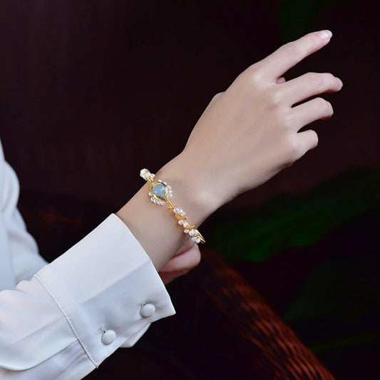 Gold-plated pearl bracelet with braided wire design and blue center gem on the wrist