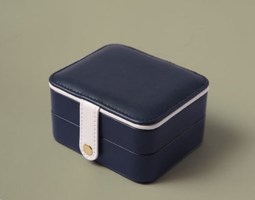 Portable jewelry box, navy blue with white strap and gold button.