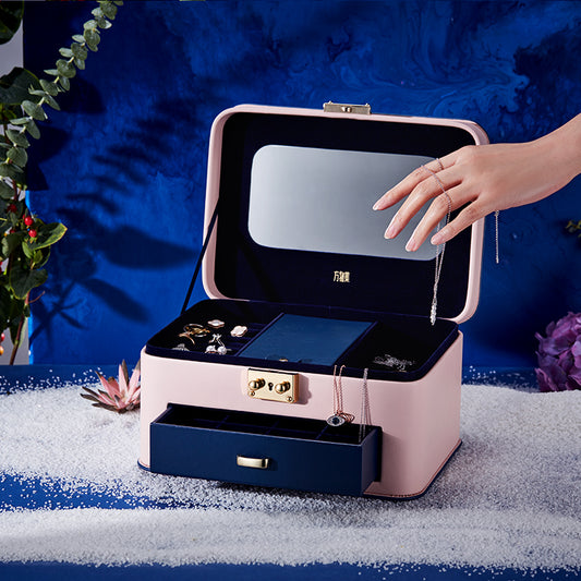 Jewelry storage box with pink exterior and navy blue interior, open to reveal jewelry and a mirror.