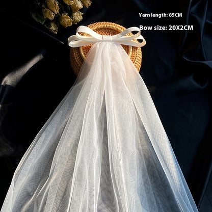 Bow veil with white tulle and satin bow, displayed on a wicker basket, CJ brand wedding accessory