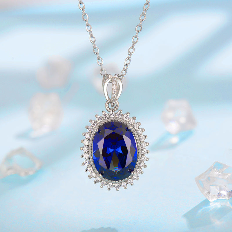 Sapphire pendant necklace with an oval-cut deep blue gemstone surrounded by a diamond halo on a silver chain