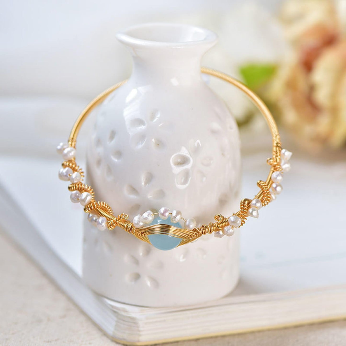 Pearl bracelet with gold-plated braided wire and turquoise centerpiece, displayed draped over a white ceramic vase