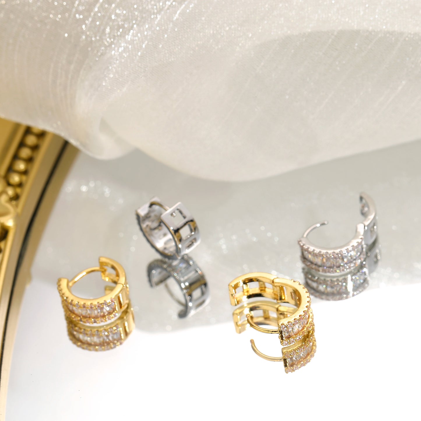 Earrings set in gold- and silver-tone with round rhinestone micro-inlays; minimalist luxury jewelry on display