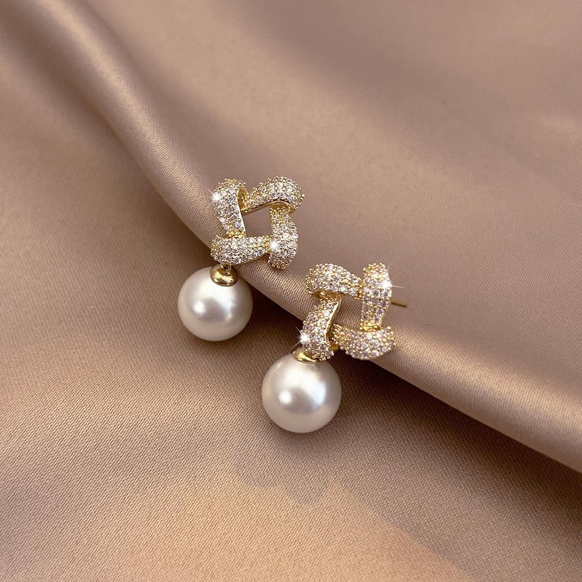 Pair of pearl earrings on a beige fabric background