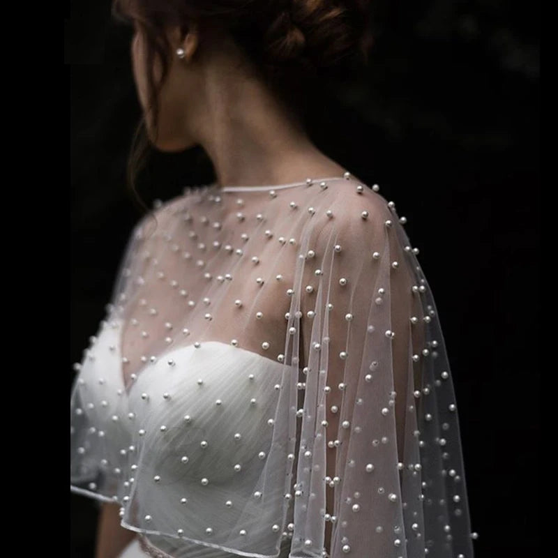 Back view of model wearing sheer pearl-embellished tulle bridal cape bolero over white strapless wedding dress