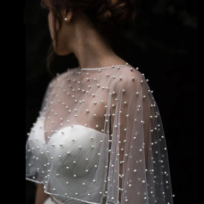 Back view of model wearing sheer pearl-embellished tulle bridal cape bolero over white strapless wedding dress