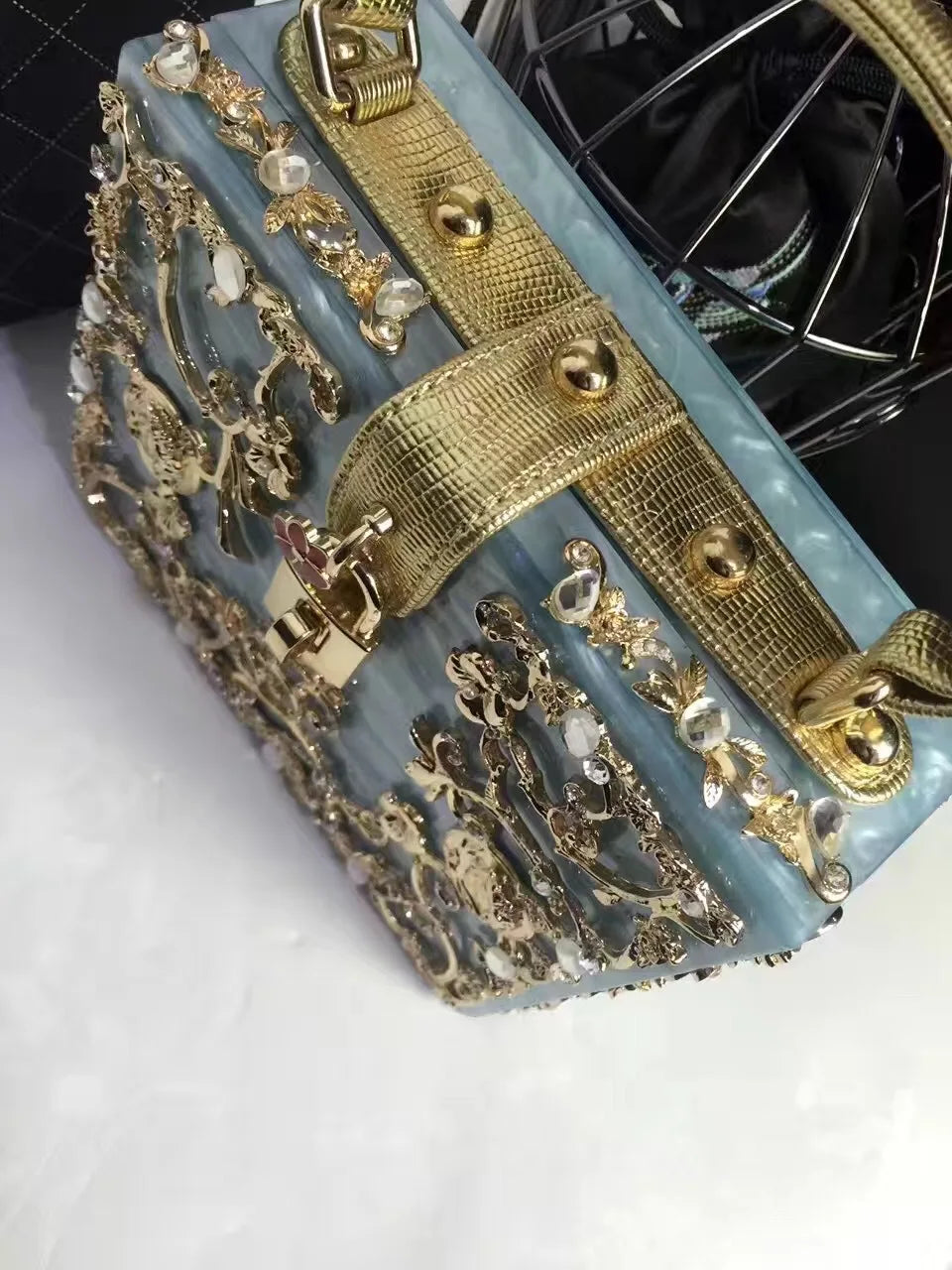 Acrylic evening bag with blue translucent body, gold rhinestone floral detailing and textured gold strap