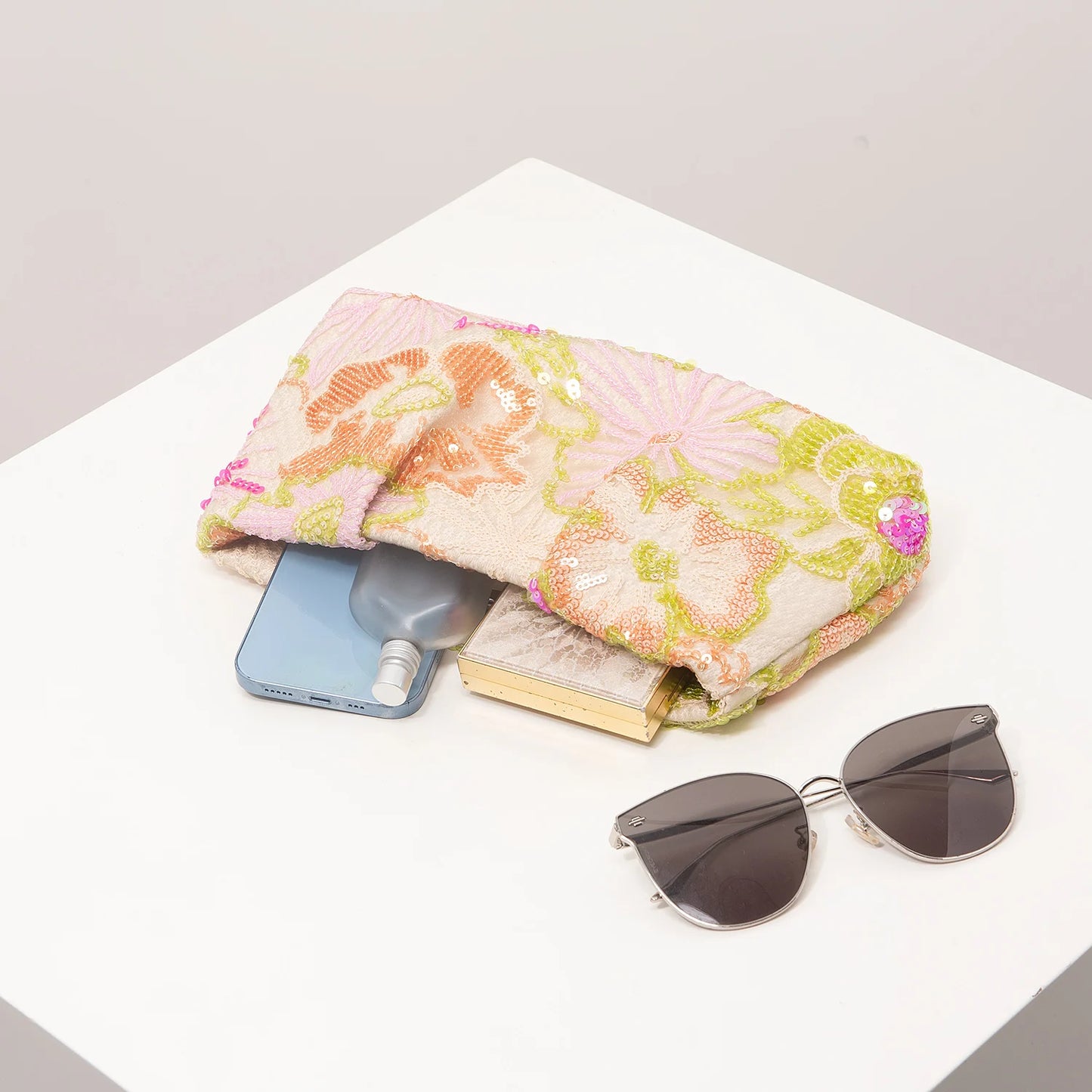 Clutch bag by Edenista with pastel floral sequin embroidery in pink and green, on table with sunglasses