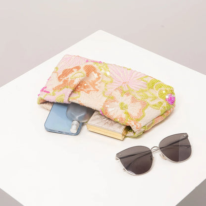 Clutch bag by Edenista with pastel floral sequin embroidery in pink and green, on table with sunglasses