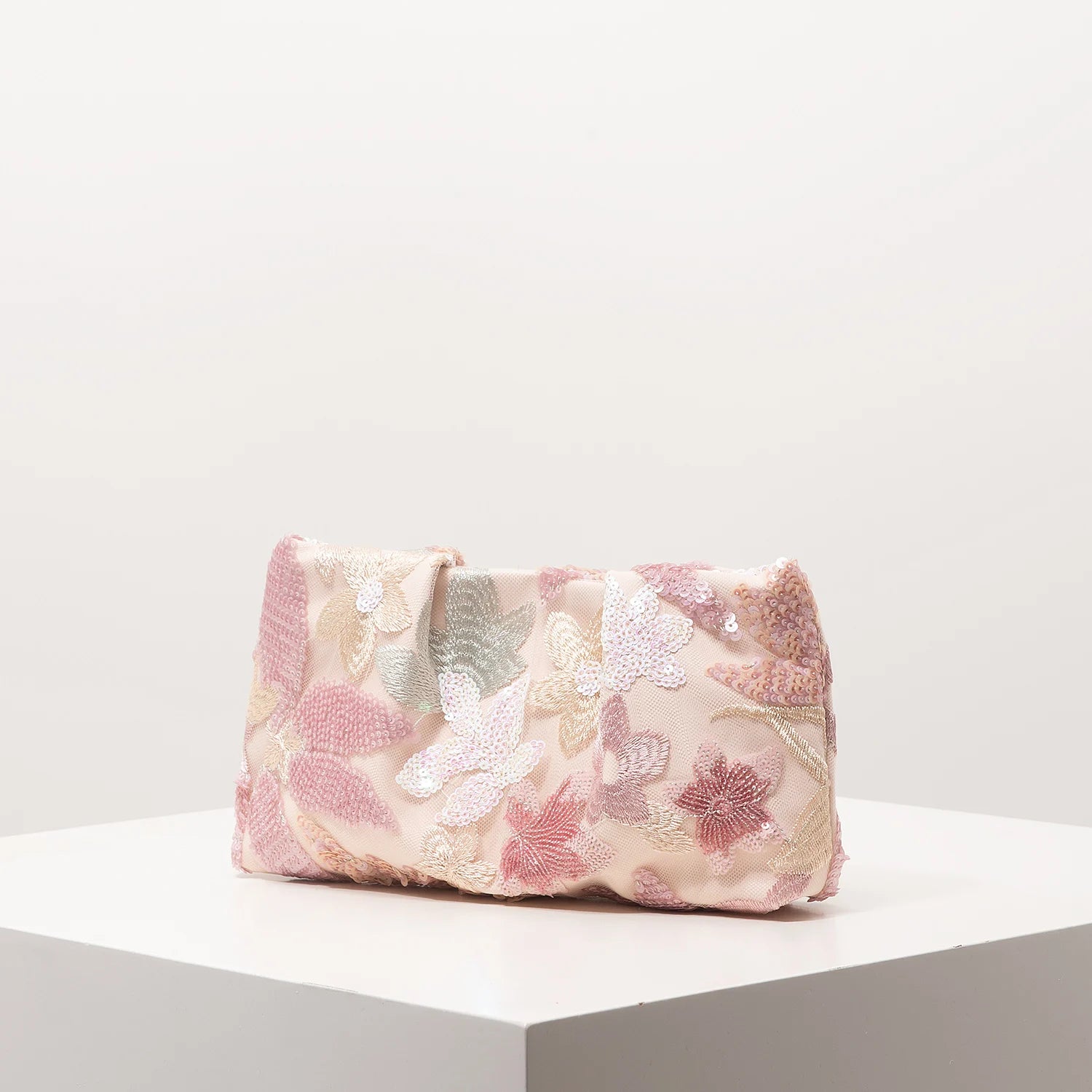 Clutch bag pink with floral embroidery and sequin details on white surface.