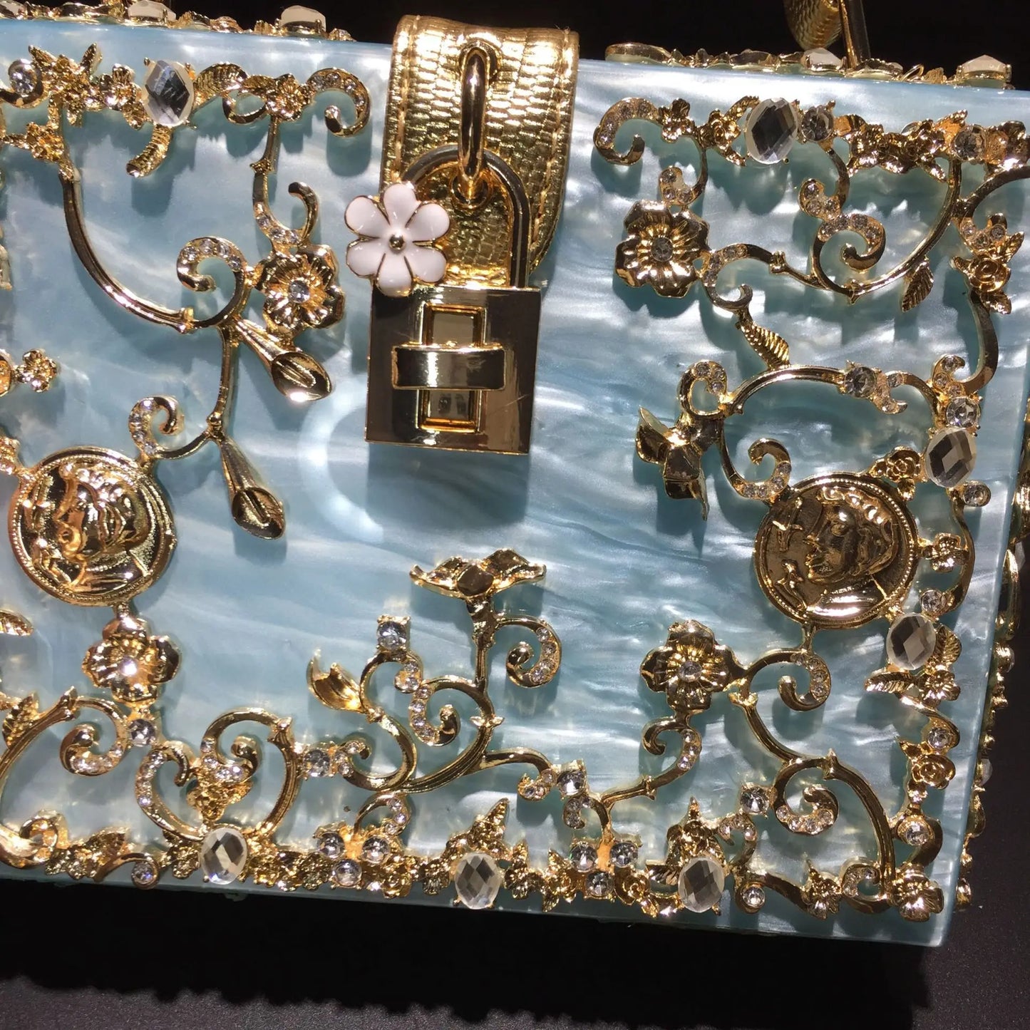 Gold acrylic evening bag with ornate floral filigree, crystal accents along the frame, and a square lock clasp.
