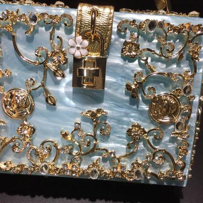 Gold acrylic evening bag with ornate floral filigree, crystal accents along the frame, and a square lock clasp.
