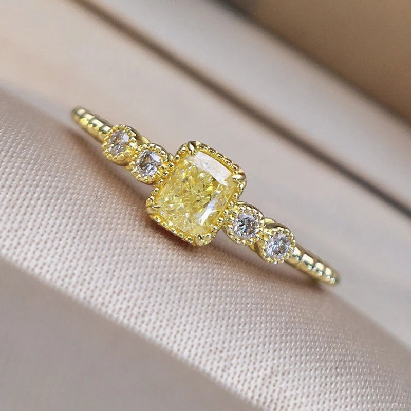 Close-up of gold ring with yellow cushion-cut CZ center stone flanked by four white round CZ stones in milgrain bezel settings on beaded band