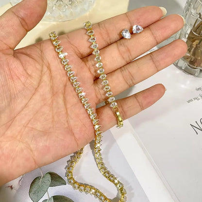 Hand holding gold-plated pear-cut CZ water drop tennis necklace with matching bracelet and stud earring on white surface
