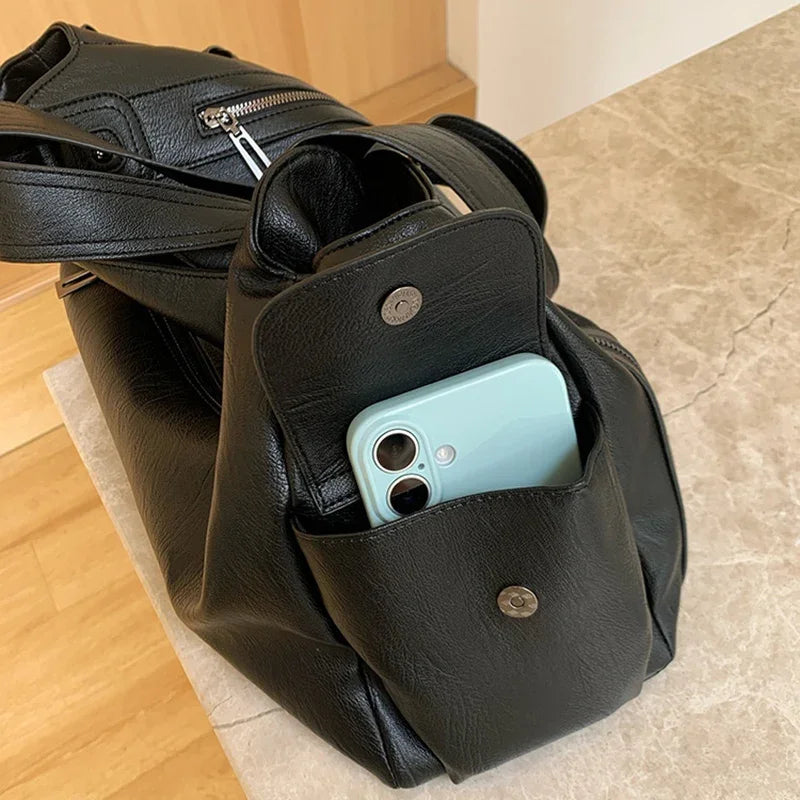 Edenista black leather tote bag with multiple pockets and shoulder straps, blue smartphone in front pocket.