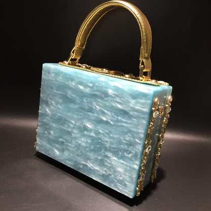 Acrylic evening bag with turquoise marbled body, gold-tone handle and rhinestone trim.