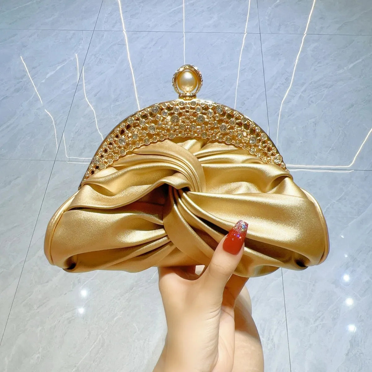 Edenista gold satin clutch with crystal-embellished arc frame and knotted bow detail