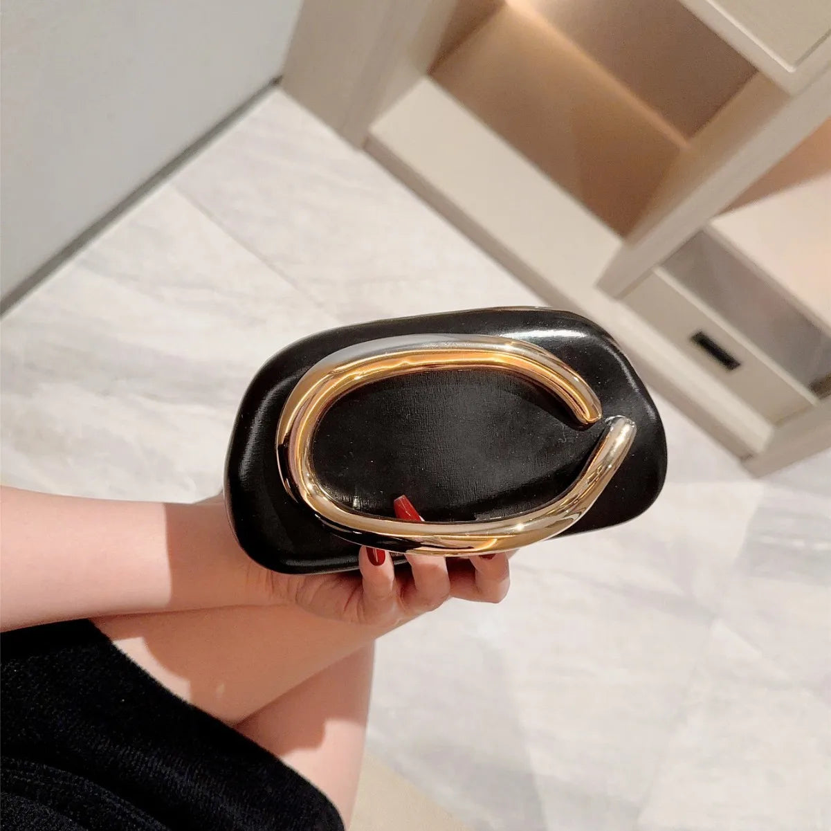 Black box clutch bag with a large gold-tone curved metal closure, held in hand.