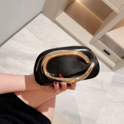Black box clutch bag with a large gold-tone curved metal closure, held in hand.
