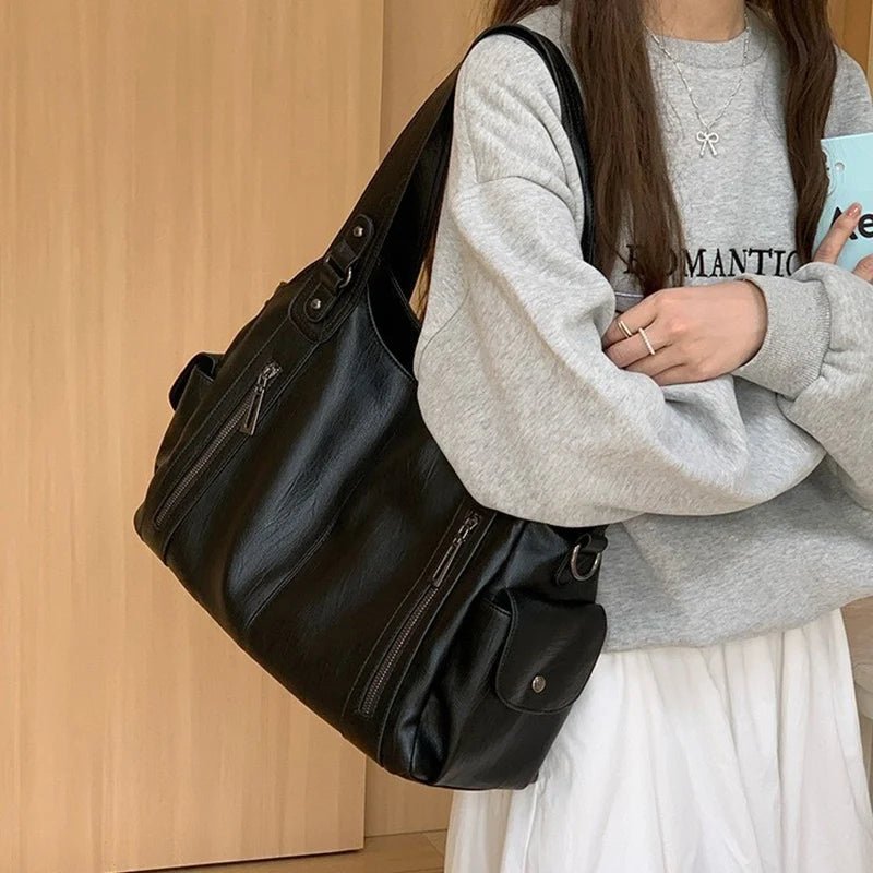 Women's black leather tote bag with large capacity and multiple zippered pockets, shoulder strap