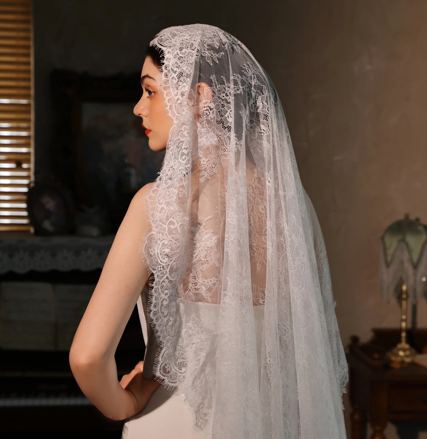 Bride in side profile wearing long white lace chapel veil with intricate floral lace border trim draping over shoulders in vintage room