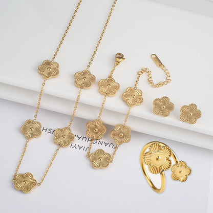 Flat lay of gold five-petal flower motif jewelry set including long necklace bracelet stud earrings and open ring on white surface