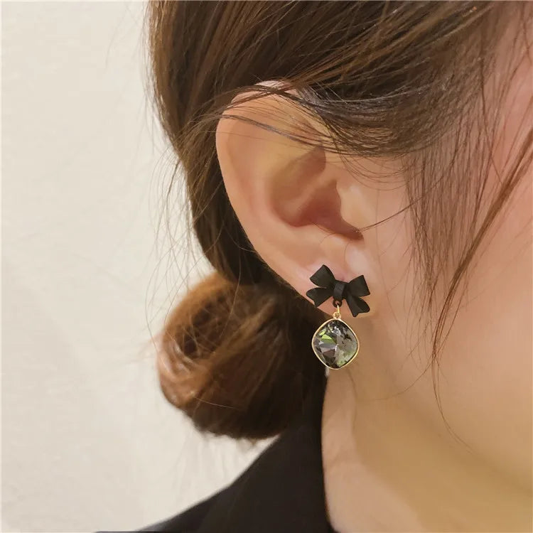 Bow-tie stud earrings in black with a gold-tone bezel gemstone pendant