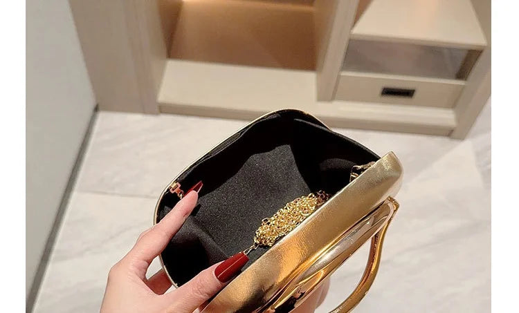 Gold metal-closure box clutch bag with black lining and chain strap, held by hand.