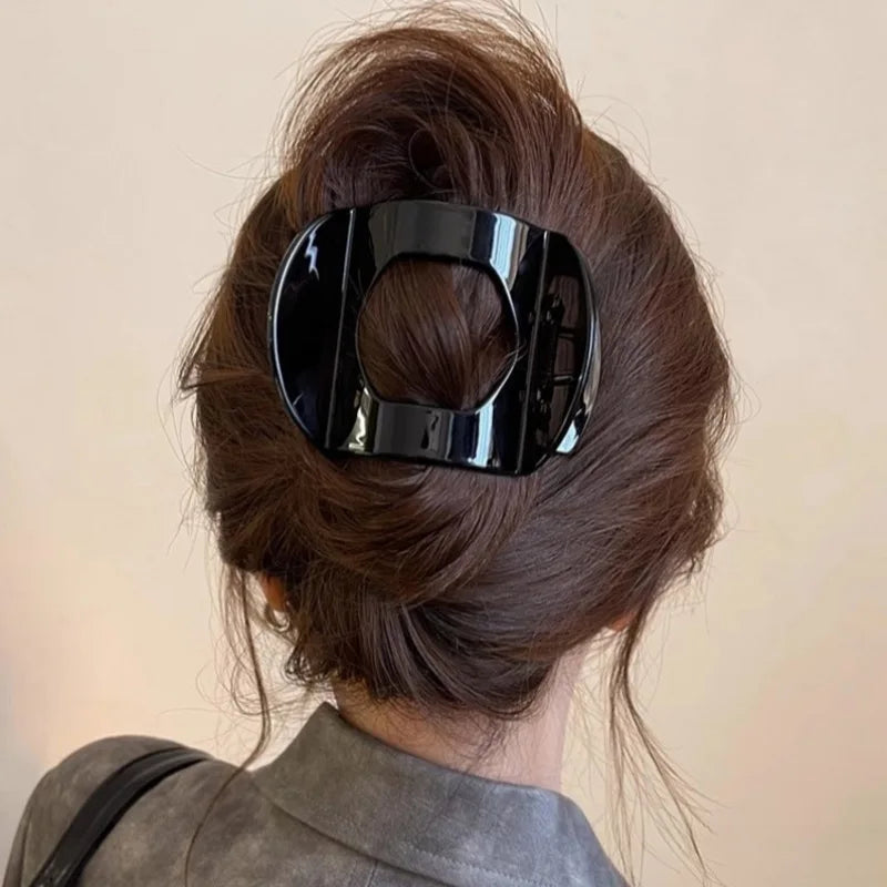 Crab hair clip in glossy black plastic with a square rounded frame, securing a voluminous brunette updo.