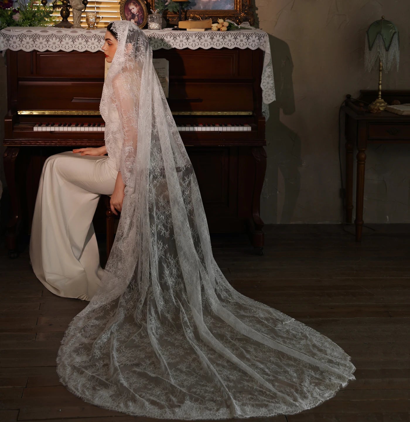 Model in white gown seated at piano with long white lace chapel veil flowing dramatically to floor showing full chapel length